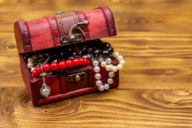 Cofre del tesoro vintage lleno de joyas y accesorios sobre fondo de madera