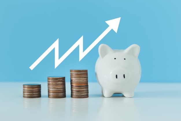 Cofrinho branco e moedas de dinheiro de pilha com gráfico crescente na mesa azul economizando para dinheiro futuro investimento conceito de negócios de investimento