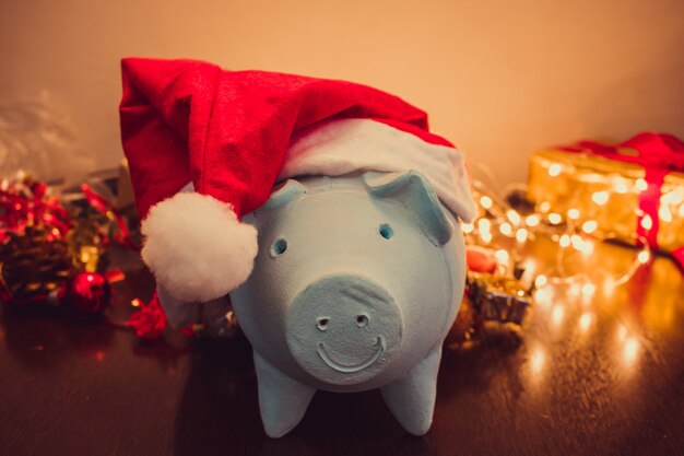 Cofrinho com chapéu de Papai Noel no fundo desfocado de Natal com enfeites de Natal, presentes e luz. Espaço para texto.