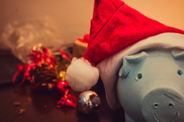 Cofrinho com chapéu de Papai Noel no fundo desfocado de Natal com enfeites de Natal, presentes e luz. Espaço para texto.