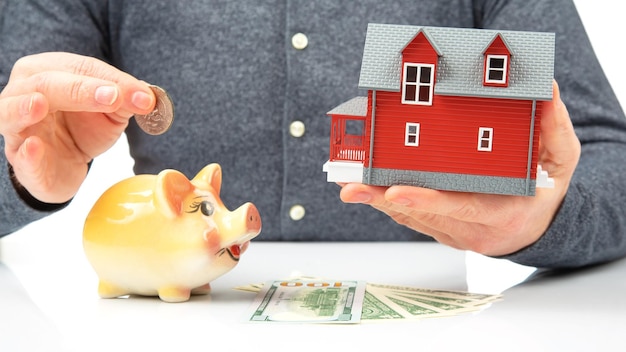 Cofrinho com dinheiro e um modelo de uma casa nas mãos de um homem o conceito de acumular finanças para comprar uma casa