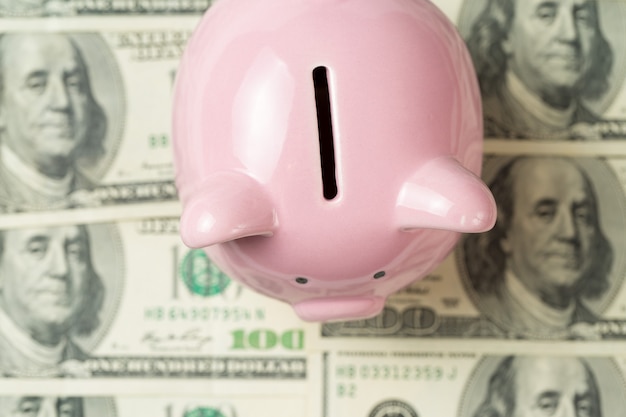 Foto cofrinho de porco no fundo de 100 notas de dólar americano. conceito de riqueza e troca.
