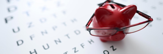 Cofrinho de porco vermelho em óculos fica na mesa oftalmológica closeup
