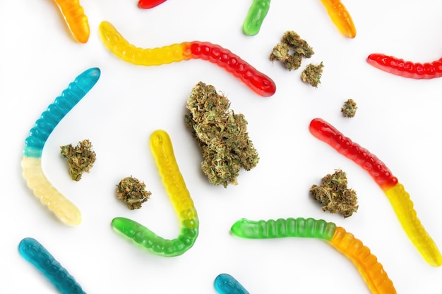 Cogollos de marihuana secos y gusanos de mermelada de diferentes colores yacen sobre un fondo blanco Vista desde arriba