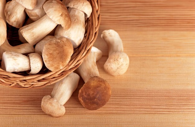 Cogumelos brancos crus na cesta na mesa de madeira