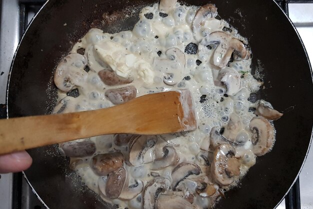 Cogumelos cozinhando em uma panela de Teflon com creme de leite e uma colher de pau