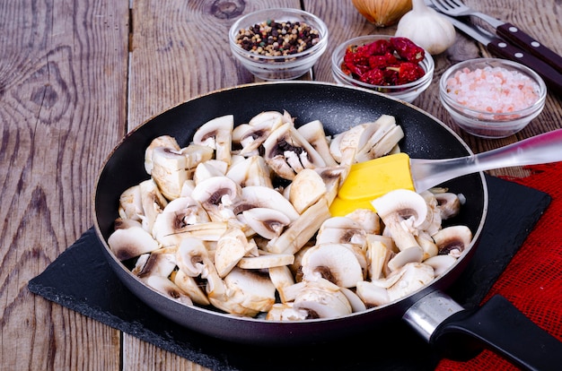 Cogumelos crus fatiados na frigideira na mesa de madeira.