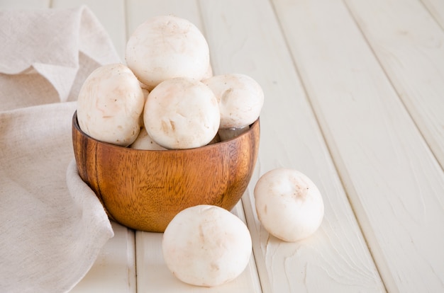 Cogumelos crus frescos em uma bacia de madeira em um fundo branco com espaço para o texto.