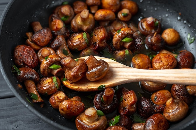 Cogumelos em óleo de girassol em uma colher de pau de frigideira com cogumelos fritos