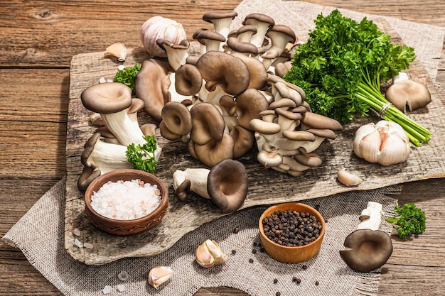 Cogumelos ostra prontos para cozinhar Especiarias frescas de salsa e alho Sombras escuras de luz forte na moda antigo fundo de madeira fechado