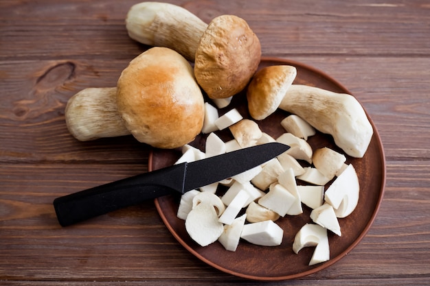 Cogumelos porcini cortados e inteiros crus bonitos em um prato marrom com uma faca em uma mesa de madeira