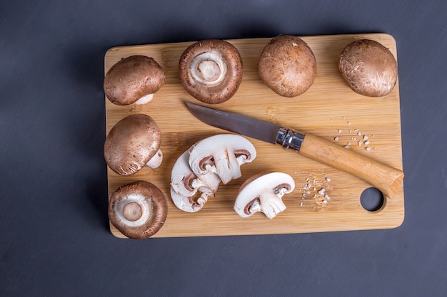 Cogumelos reais Cogumelos champignon parisienses em uma tábua de cortar de madeira de bambu. Fundo de madeira escura