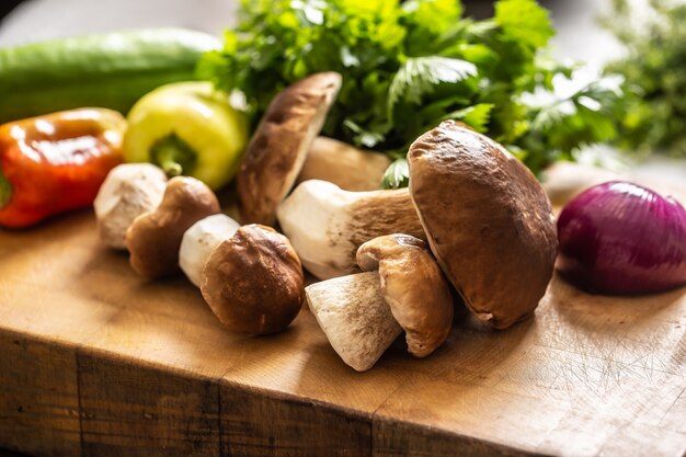 Cogumelos selvagens, cebolas, pimentões e ervas em uma mesa de madeira.