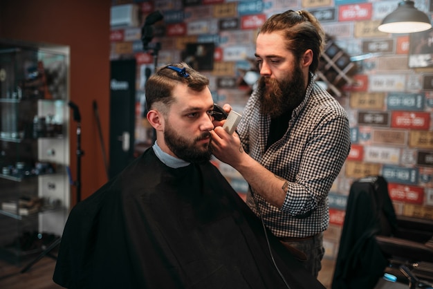 Coiffeur schneidet Haare des Kundenmannes im schwarzen Salonumhang.