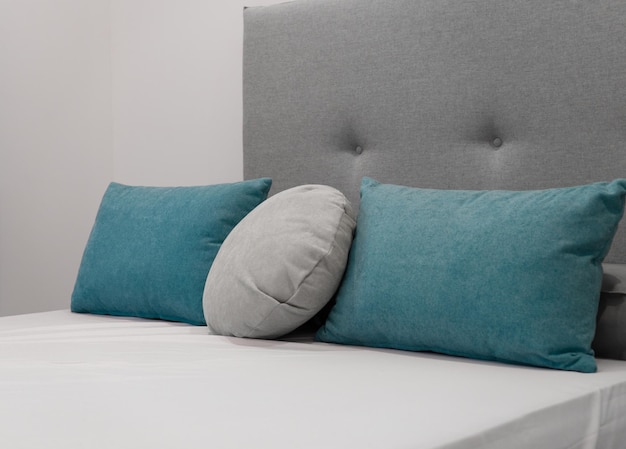 Cojines color aguamarina sobre una cama con un cabecero gris claro detrás