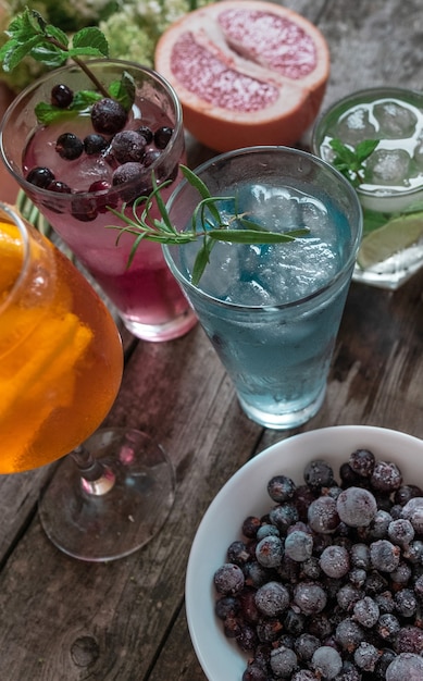 Coktail Gin Tonic, Mojito e Aperol Spritz com menta, gelo, limão, frutas, toranja e laranja no fundo de madeira.