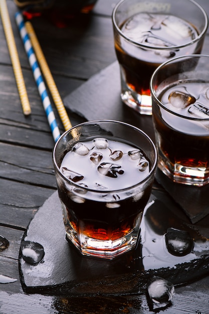 Cola con cubitos de hielo en copas en mesa de madera oscura