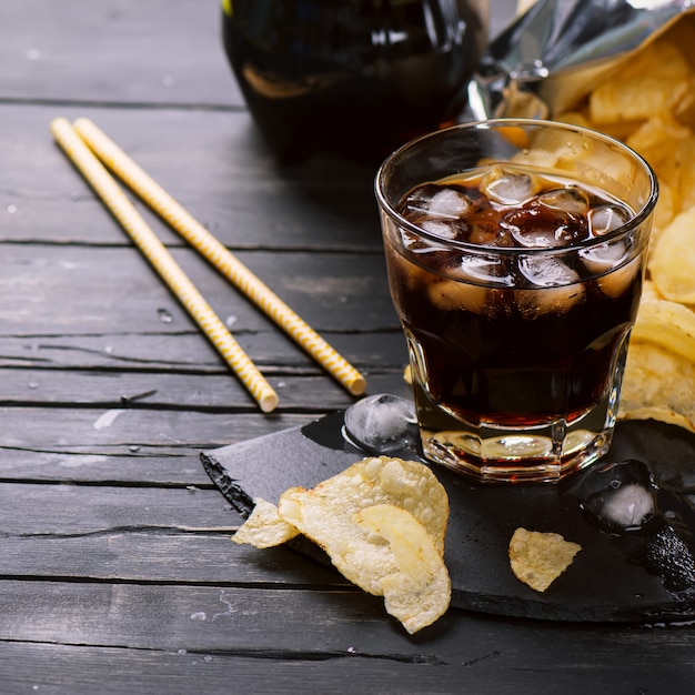 Cola con cubitos de hielo en vaso y papas fritas.