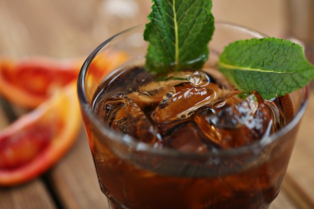 Cola de uísque cocktail com gelo em um copo. Em uma placa de madeira são fragmentos de frutas. Foto com profundidade de campo.