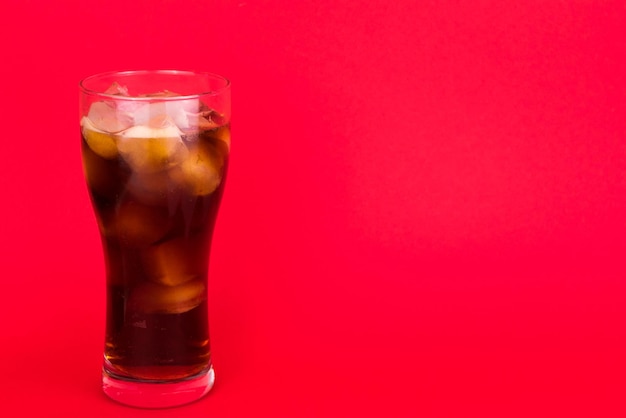 Foto cola con hielo en un vaso grande sobre un fondo rojo copiar espacio