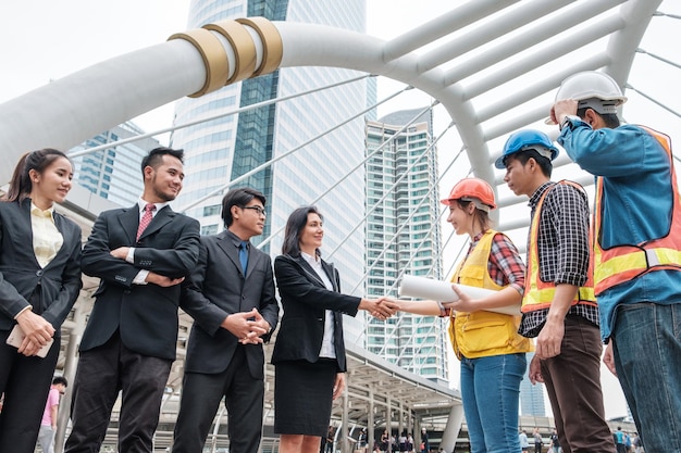 Colaboración de un grupo multiétnico de ingenieros y apretón de manos de empresarios con acuerdo de contrato de gran proyecto en la ciudad