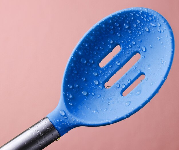 Colador de cuchara de cocina de silicona en gotas de agua sobre fondo rosa