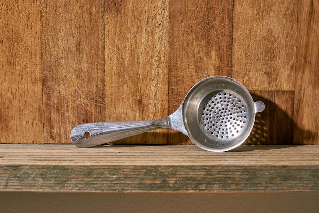 Colador de té de metal en un estante de cocina de madera.