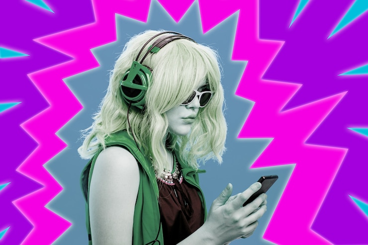 Foto colagem de arte com garota alternativa de óculos e com fone de ouvido ouve música legal em seu smartphone. mulher jovem funky em fundo multicolor de néon. imagem do conceito em estilo pop art contemporâneo.