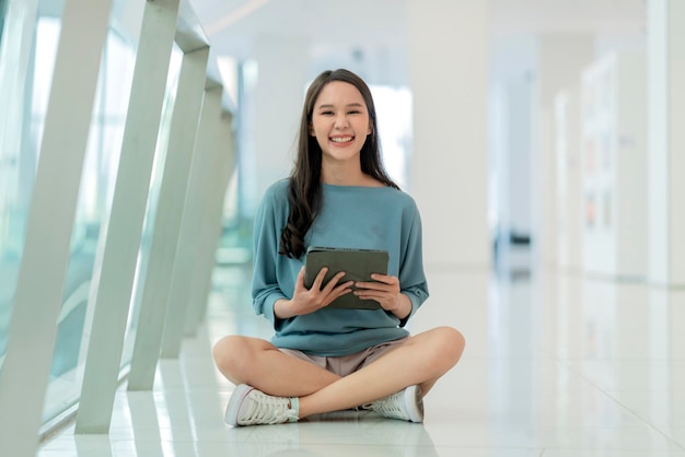 Foto colagem feminina asiática jovem mulher do campus sentada no chão do shopping usando tablet navegando dados de surf online mídia social com diversão alegre sorridente mulher asiática nômade digital sente-se no chão trabalho casual online