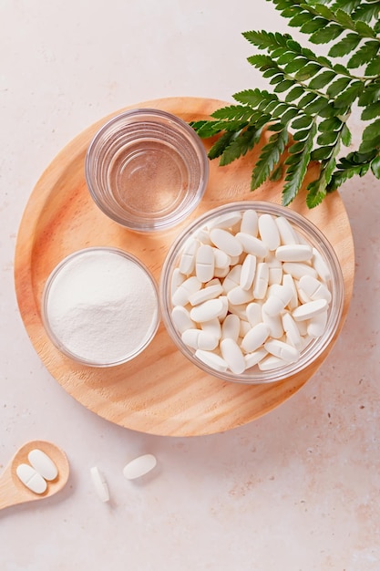 Colágeno en polvo vaso de agua y pastillas de colágeno sobre fondo beige neutro Suplementos de colágeno en diferentes formas para un espacio de copia de piel hermosa y joven