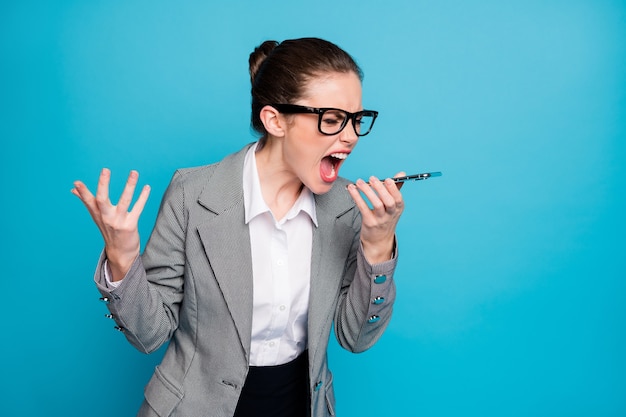 Colarinho de menina irritada e frustrada gritar viva-voz telefone inteligente usar jaqueta blazer isolado fundo de cor azul