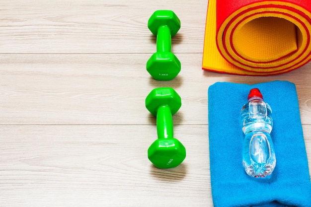 Colchoneta de yoga una toalla una botella de agua y pesas en una habitación o un gimnasio en el suelo gris Vista superior