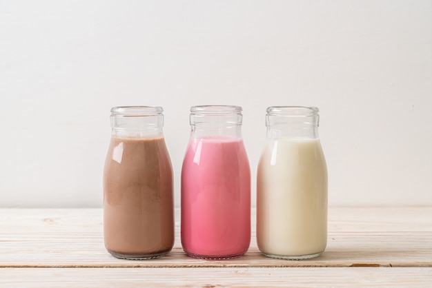 Coleção de bebidas com leite com chocolate, leite rosa e leite fresco em garrafa na mesa de madeira