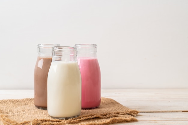 Coleção de bebidas com leite com chocolate, leite rosa e leite fresco em garrafa na mesa de madeira