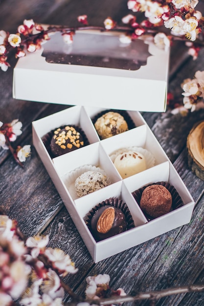 Coleção de primavera de bombons de chocolate artesanal e decoração de flores de cerejeira em fundo de madeira rústica