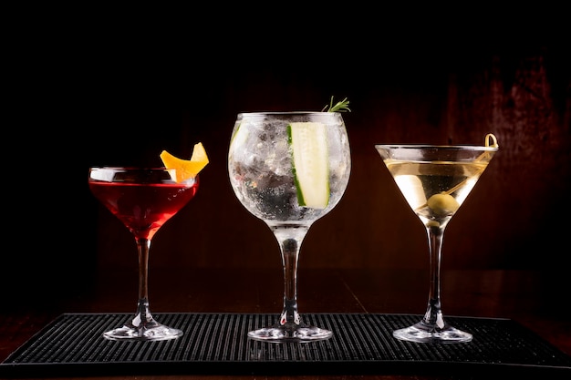 Coleção de três copos de coquetel, incluindo gin tônica martini e vesper com azeitona em suporte de borracha visto de frente