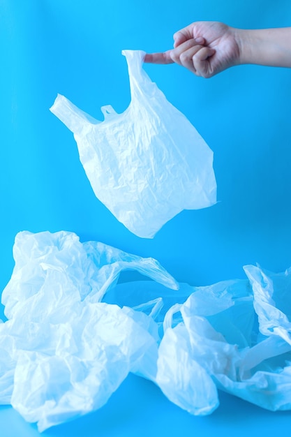 Colección de bolsas de plástico desechables transparentes con la mano sosteniendo una de ellas sobre fondo azul.