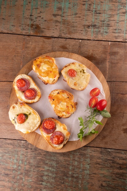 Colección de bruschetta horneada en rebanadas de pan con tomates cherry de queso derretido en totora en la vista superior de la mesa de madera en ángulo