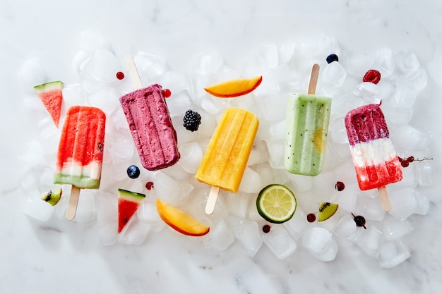 Colección de coloridos y sabrosos helados caseros en un palo con jugosas bayas y trozos de diversas frutas en cubitos de hielo. Endecha plana