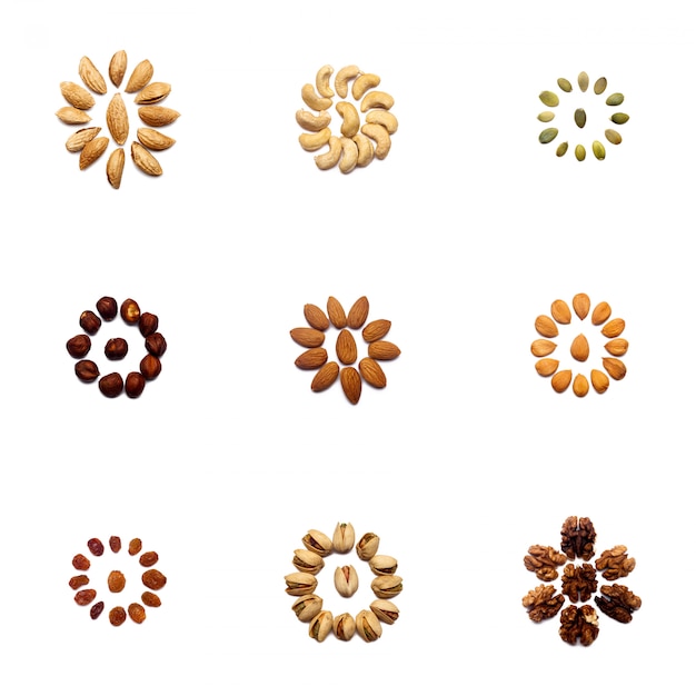 Una colección de nueces hechas de almendras, nueces, avellanas, pistachos, anacardos se encuentran en forma de círculo o sol en una pared blanca aislada. Varios patrones de nueces