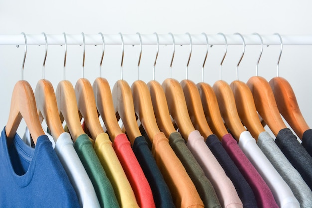 Colección de primer plano de camisetas coloridas colgadas en una percha de madera sobre fondo blanco