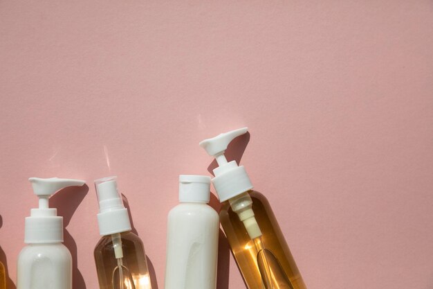 Una colección de productos cosméticos de belleza en botellas transparentes sobre un fondo rosa.