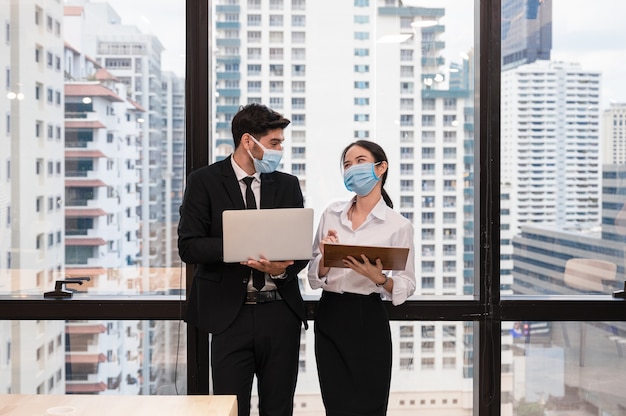 Colega de negócios multiétnico usando máscara facial e sorrindo com a discussão no novo escritório normal