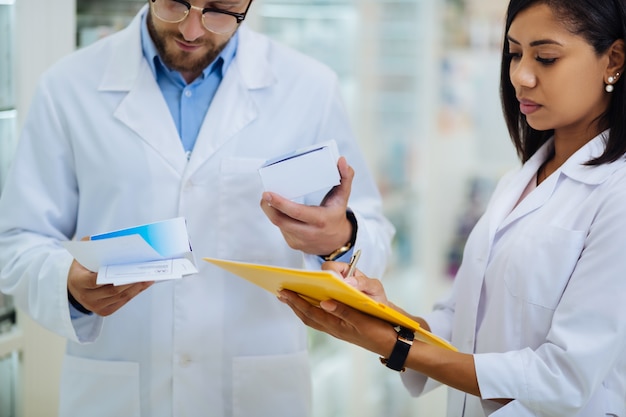 Foto colega de trabalho internacional. farmacêutico barbudo sério curvando a cabeça enquanto verifica os componentes