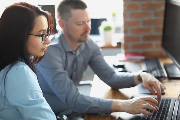 Un colega masculino ayuda a una compañera de trabajo con el trabajo a explicar en la corporación de la vida de la oficina de la computadora portátil