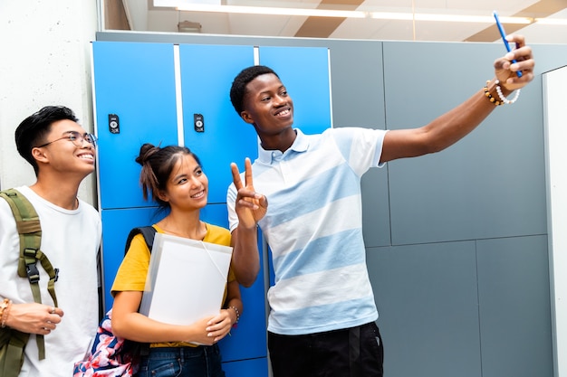 Colegas adolescentes multirraciais tirando uma selfie no corredor do colégio Copiar o espaço Voltar para a escola