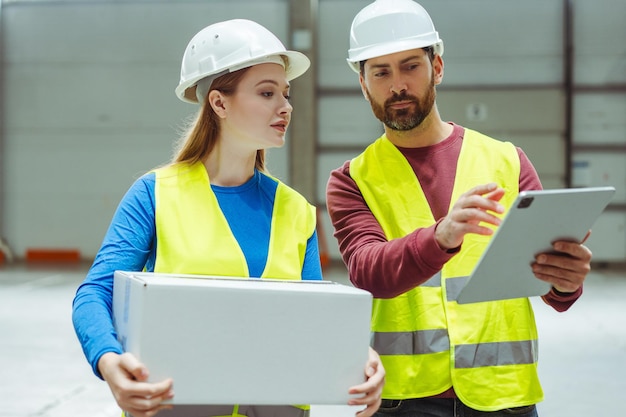 Colegas con cascos y ropa de trabajo mujer sosteniendo caja con maqueta de capataz profesional