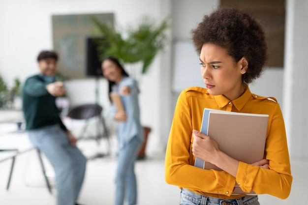 Foto colegas de grupo intimidando e rindo de uma triste senhora negra no corredor da universidade chateada aluna