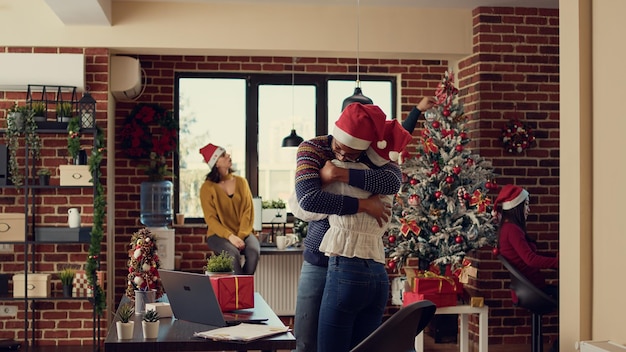 Colegas de inicialização dando presentes na véspera de natal, comemorando a festividade do feriado de inverno no escritório decorado com luzes e árvores. Homem e mulher trocando presentes durante a celebração do natal.