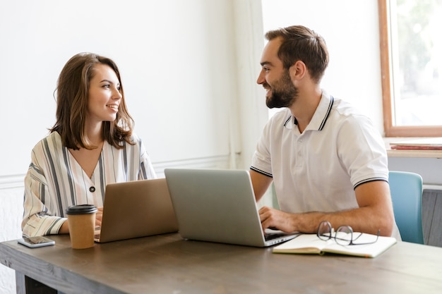 colegas de jovem casal positivo feliz trabalham com computadores laptop dentro de casa no escritório.